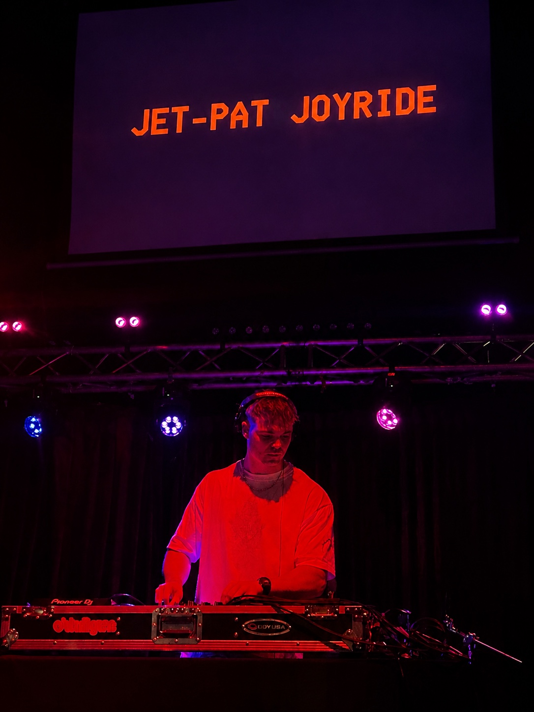 Jet-Pat Joyride mixing on stage beneath purple and red club lights